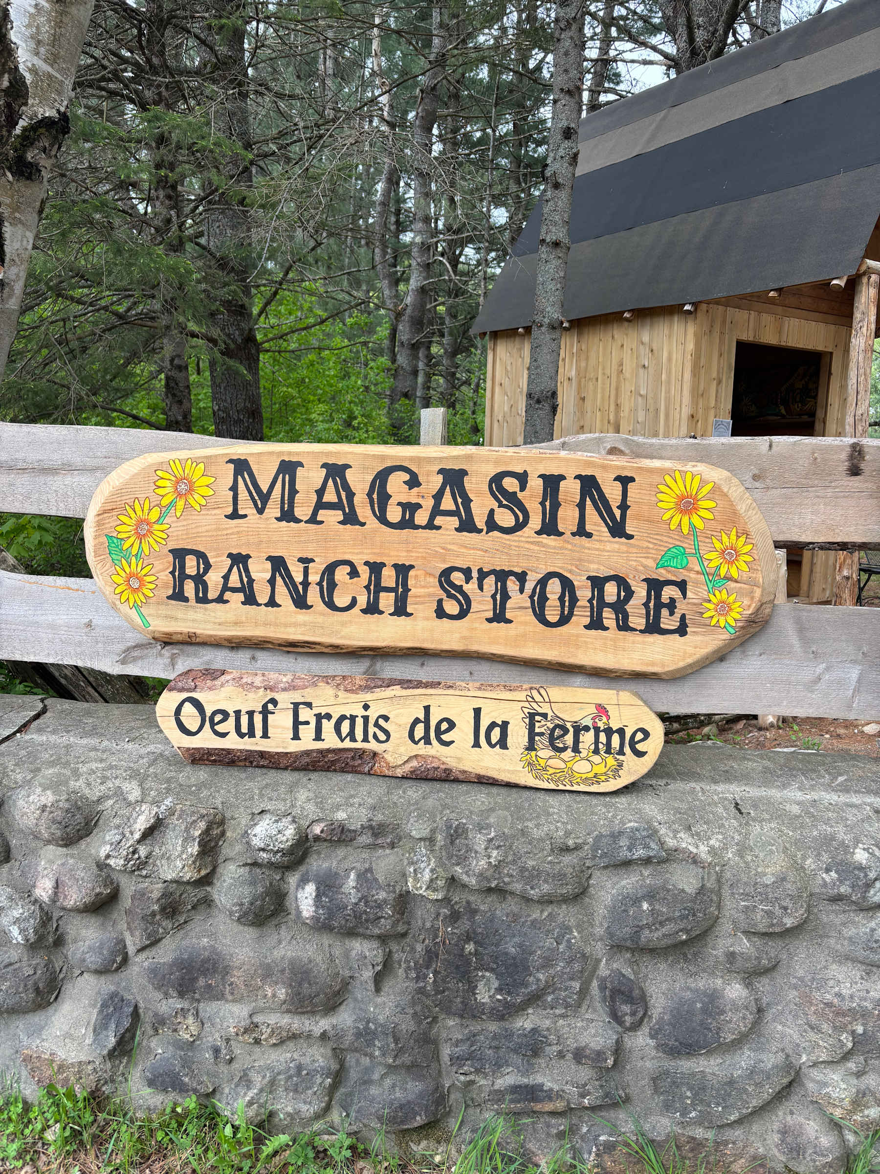 Hand-painted wooden signs reading Magasin Ranch Store and Oeuf Frais de la Ferme, in front of the timber farm store