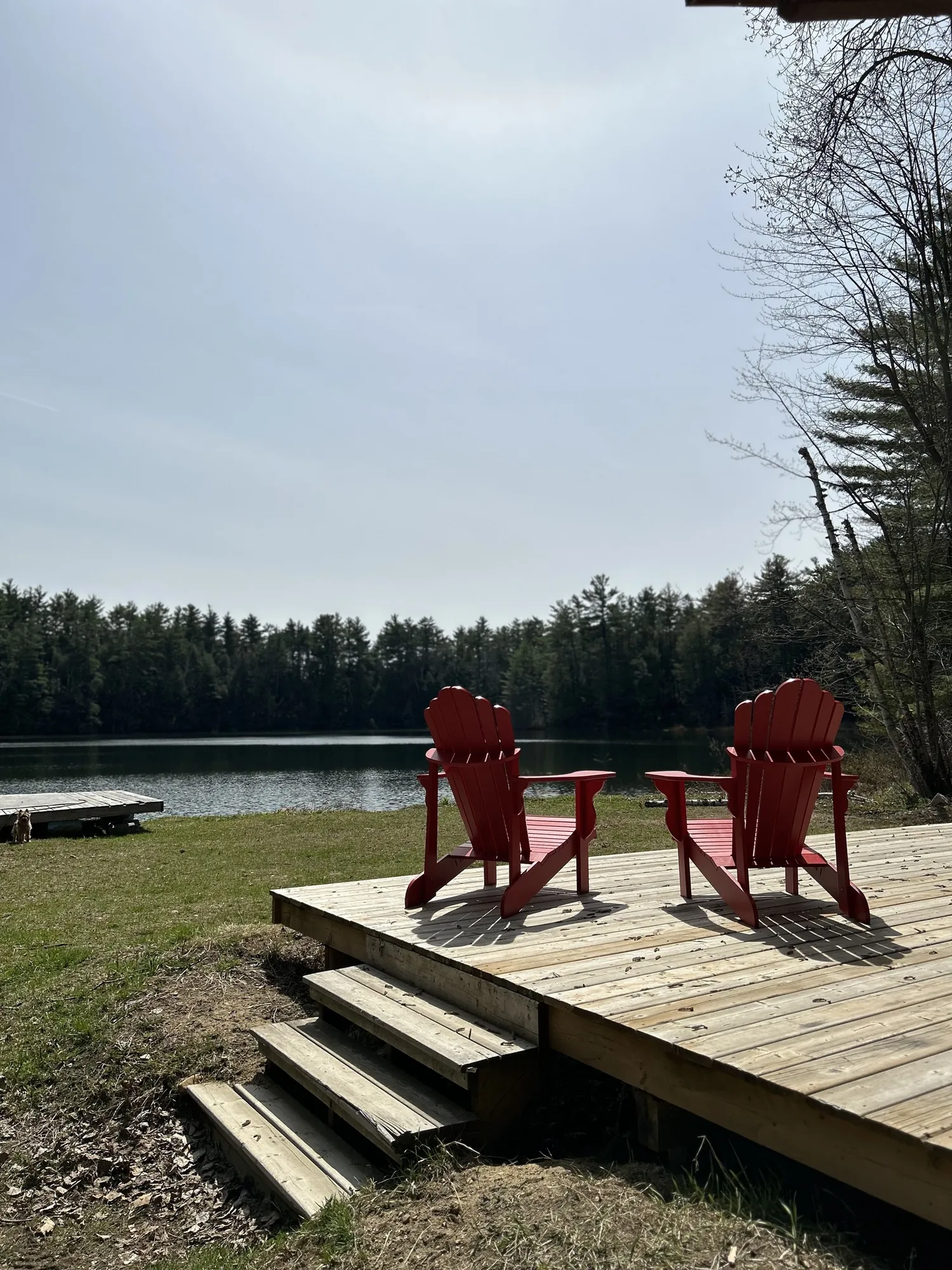 Two red Adirondack chairs on a wooden deck overlooking the lake