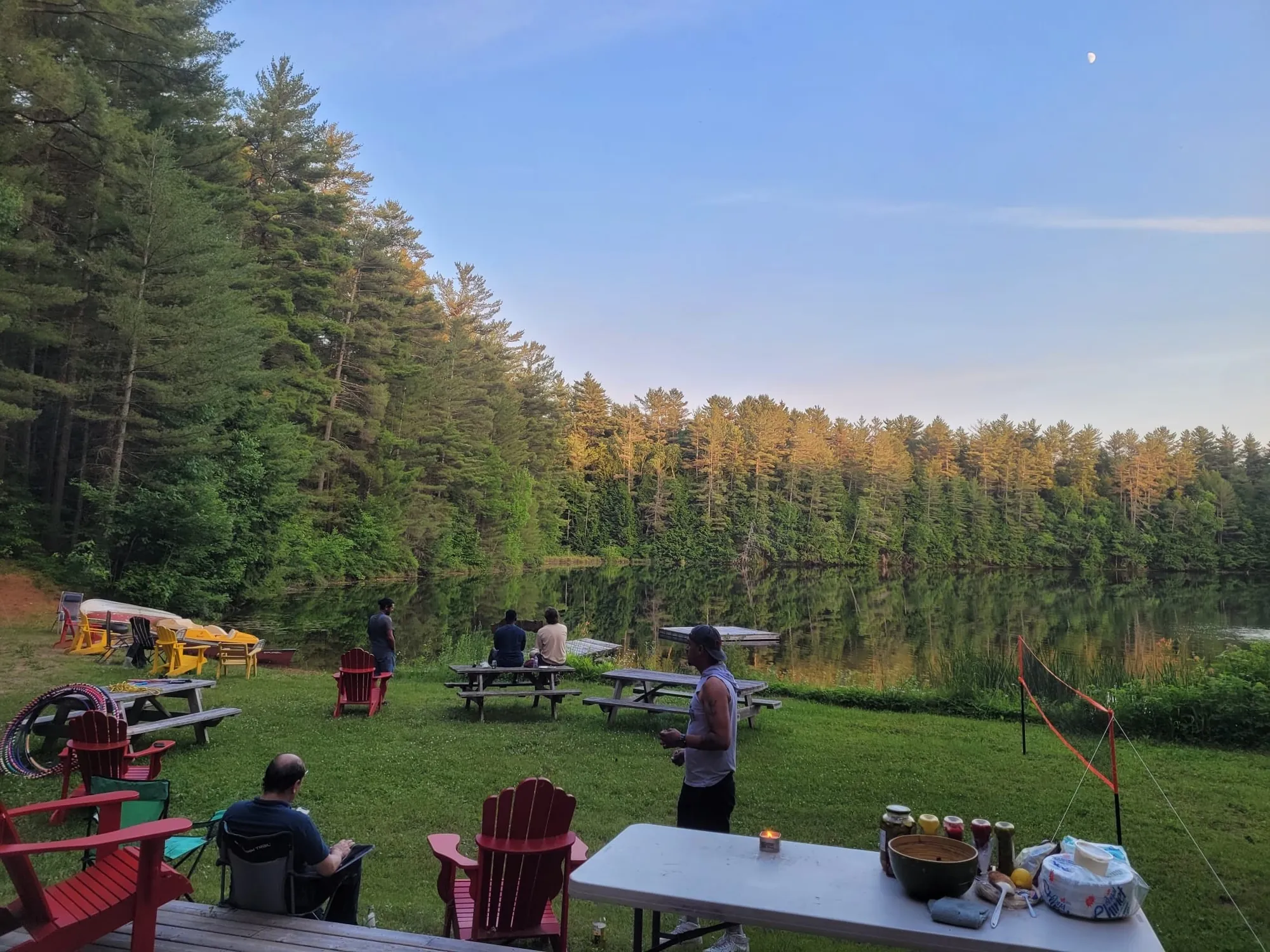 Guests relaxing in red Adirondack chairs on the lawn above Pine Lake at golden hour
